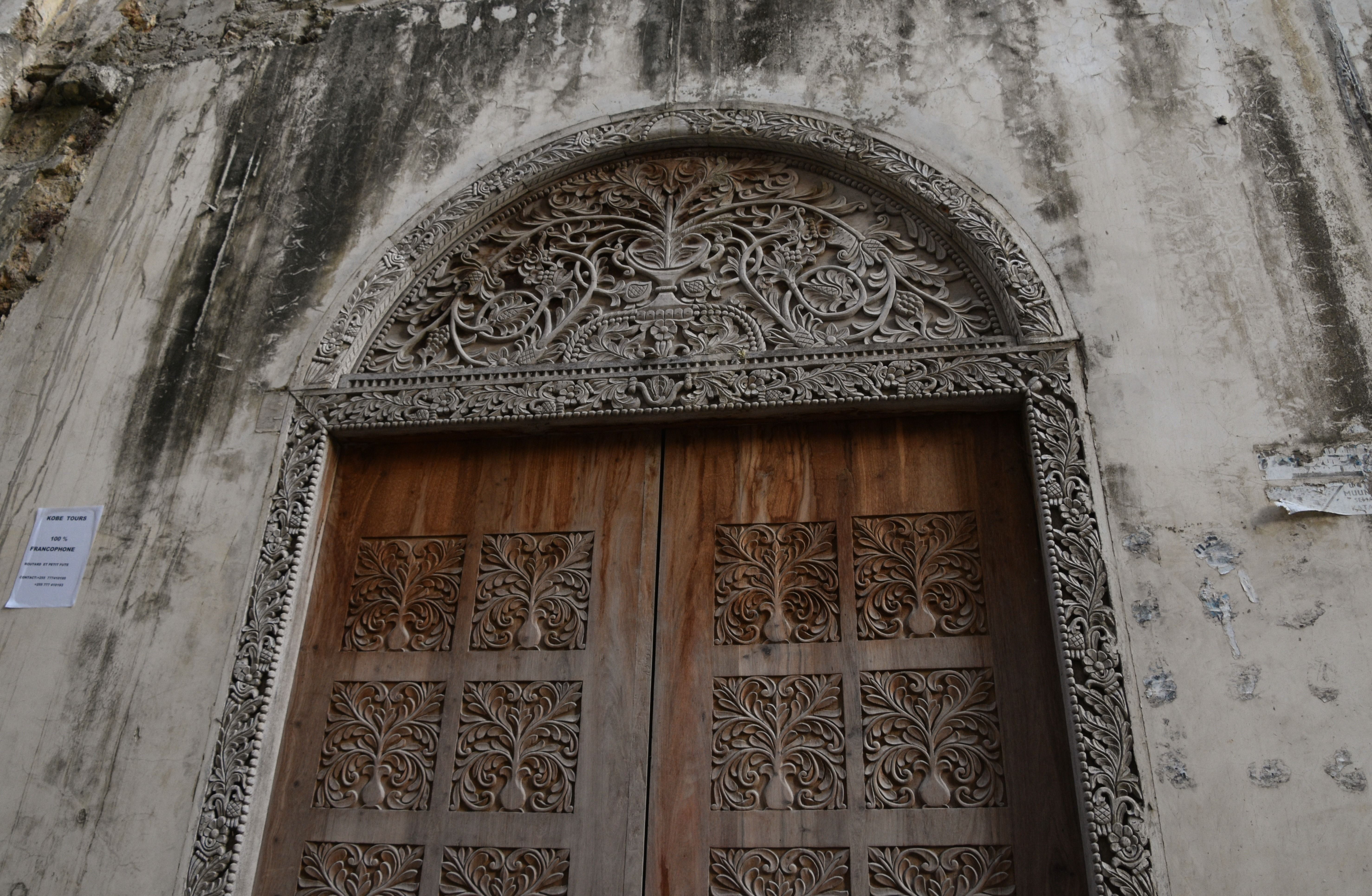 A carved wooden Zanzibar door with a foliate arch and tree-of-life panels in Stone Town.