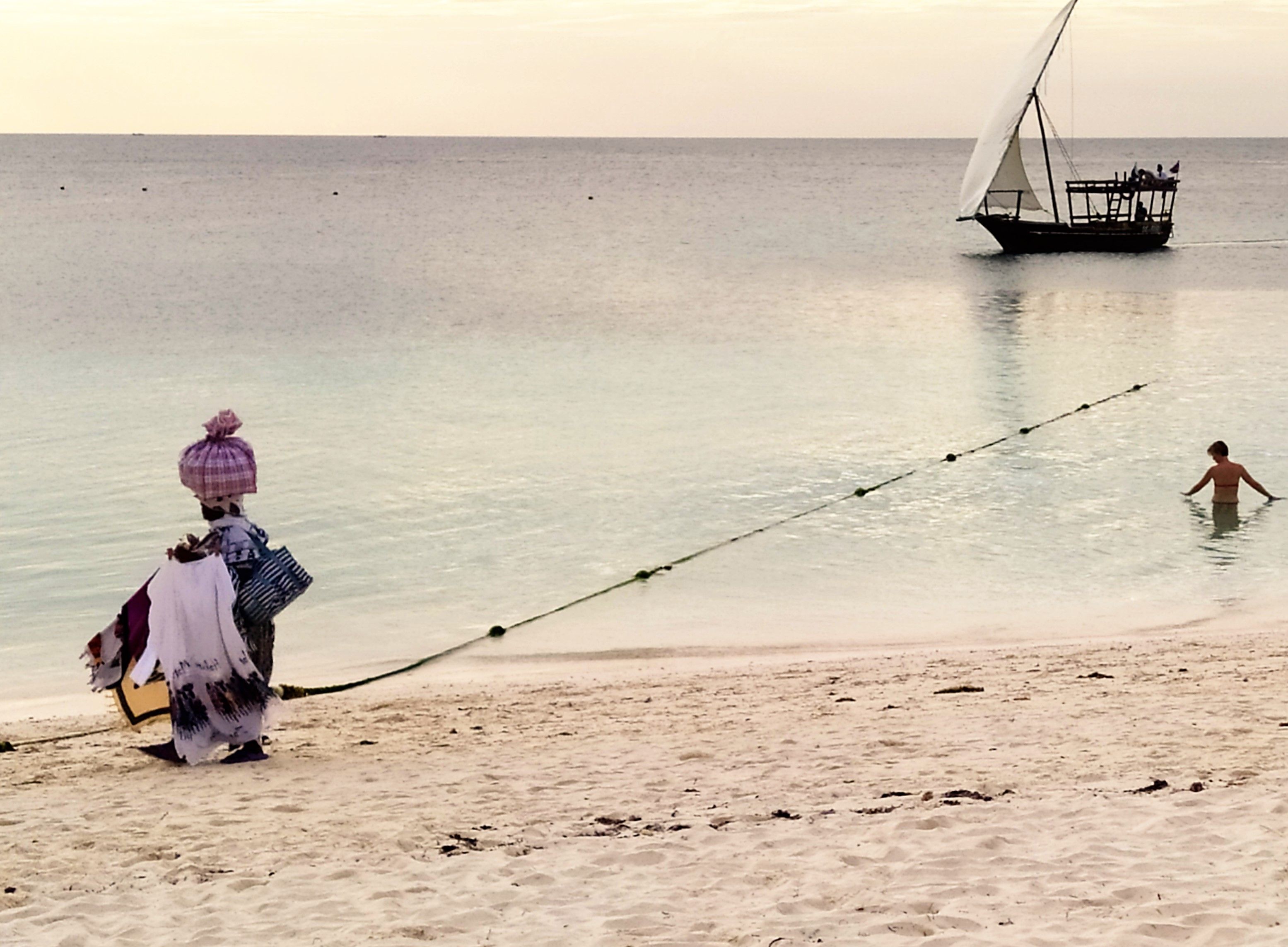 A traditional dhow under sail off the white-sand beach at Kendwa at golden hour, Zanzibar.