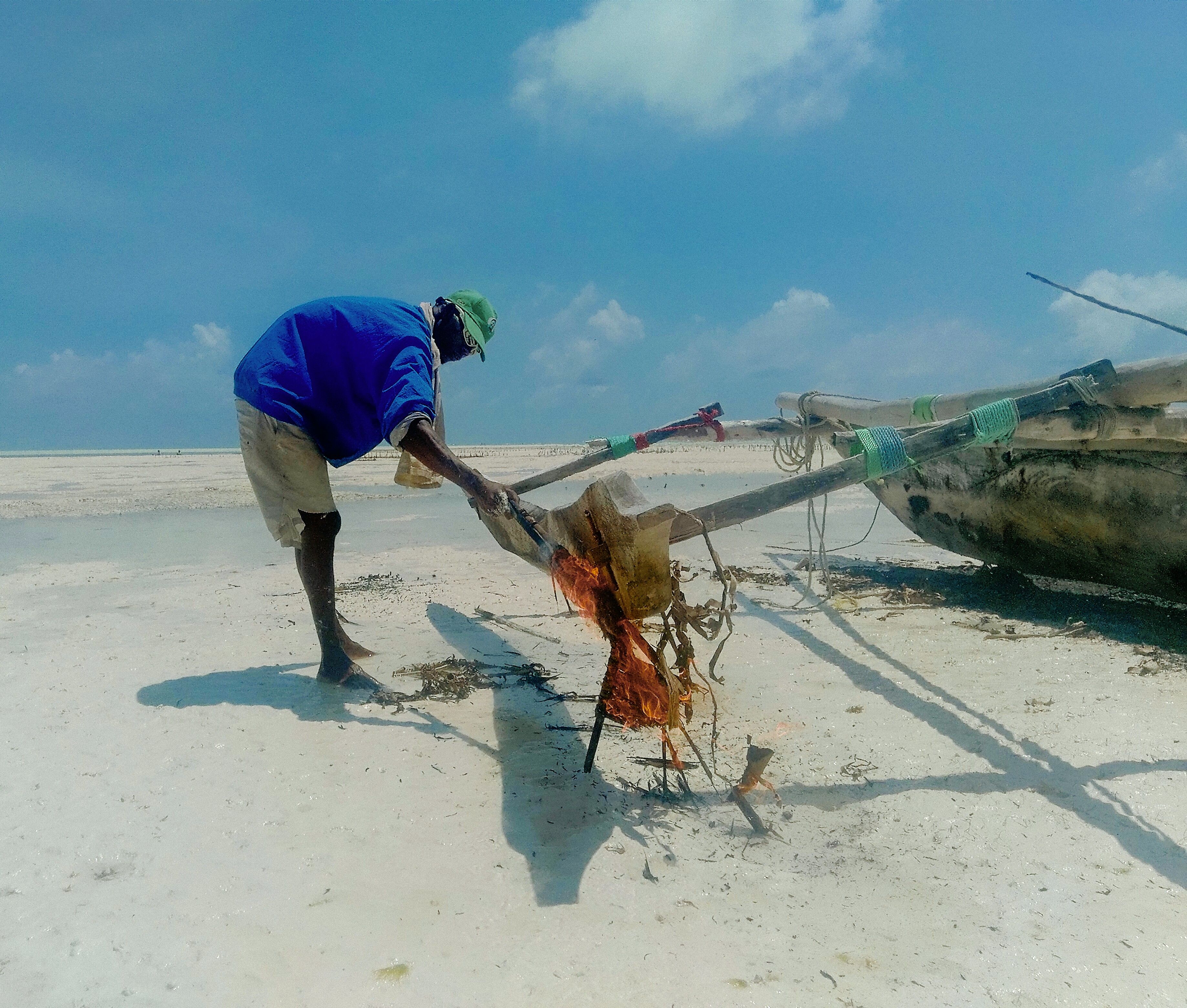 A fisherman working on his beached wooden dhow on the open low-tide sand at Jambiani on Zanzibar's southeast coast, the honest working-village character of this stretch of coast.