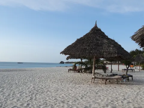Calm beach at Kendwa on Zanzibar's north coast, with a thatched sun shade and wooden loungers on pale sand and flat blue sea beyond