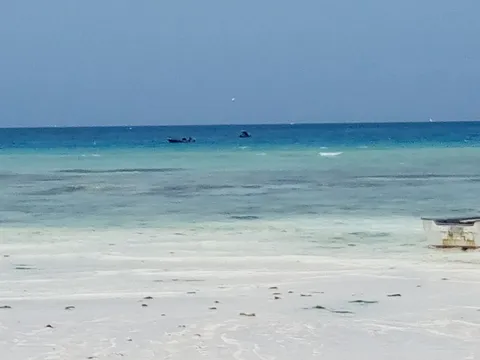 Wide white-sand beach at Nungwi on Zanzibar's north tip, with clear turquoise water deepening to blue and small boats moored offshore