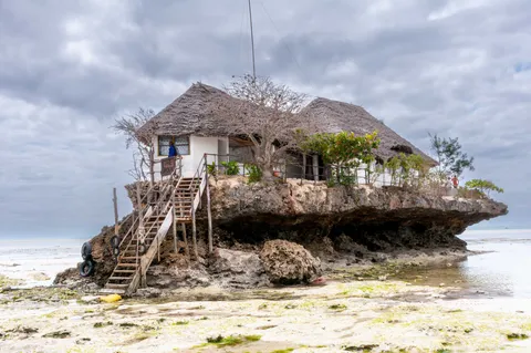 The Rock restaurant on its coral outcrop at low tide off Pingwe on the Michamvi peninsula, Zanzibar, with wooden steps up to the thatched building and the exposed reef flat around it