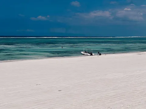 Quiet white-sand beach at Matemwe on Zanzibar's northeast coast, with rippled low-tide sand, turquoise reef flats, a small boat offshore and the reef break on the horizon