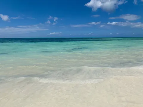 Clear turquoise water over the reef flat off Kiwengwa on Zanzibar's east coast, with white sand in the foreground under a blue sky with clouds