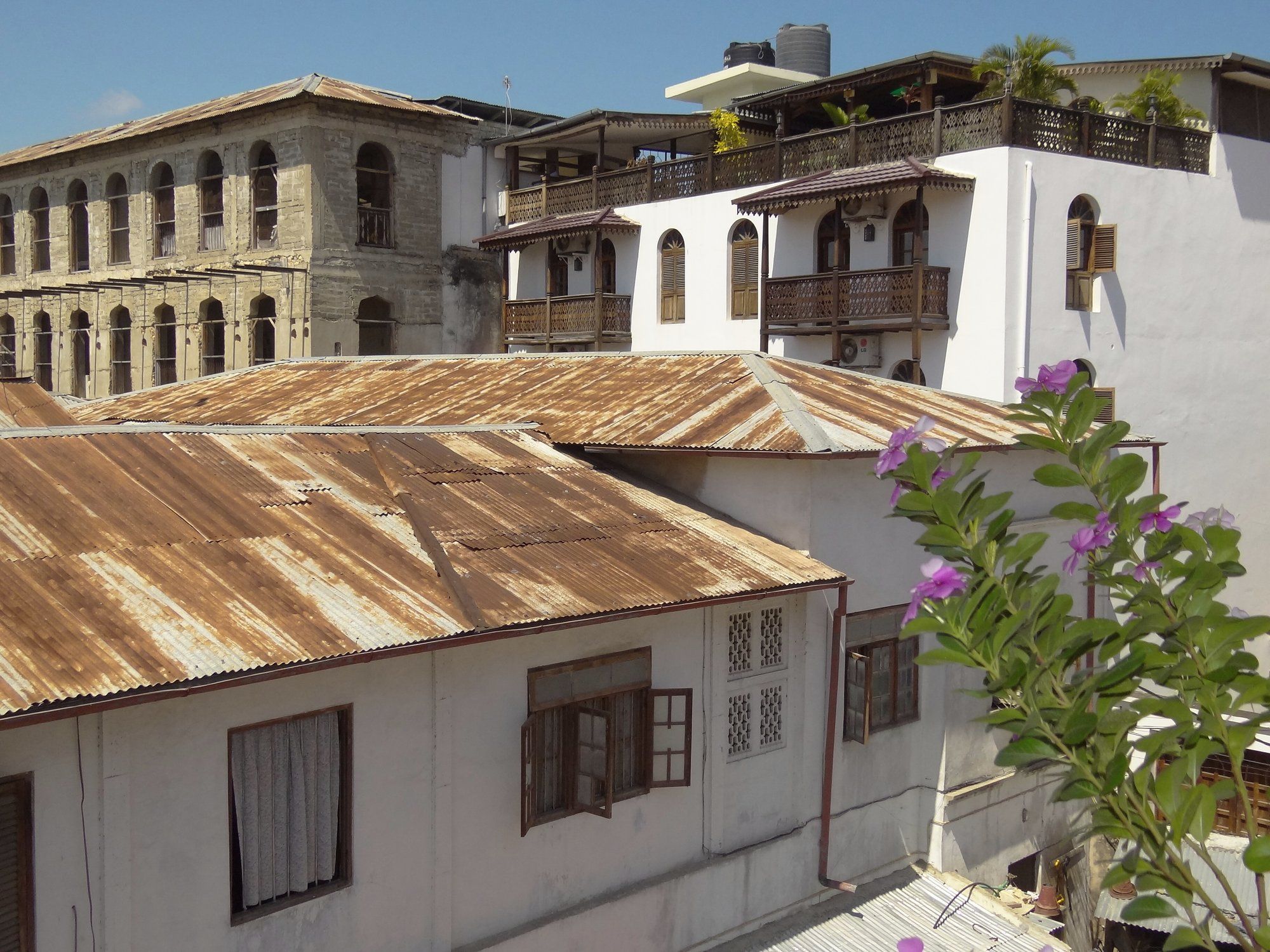 A rooftop view across the corrugated-iron roofs and carved wooden balconies of Stone Town, Zanzibar, where many of the old quarter's best tables are rooftop and terrace restaurants with harbour views.