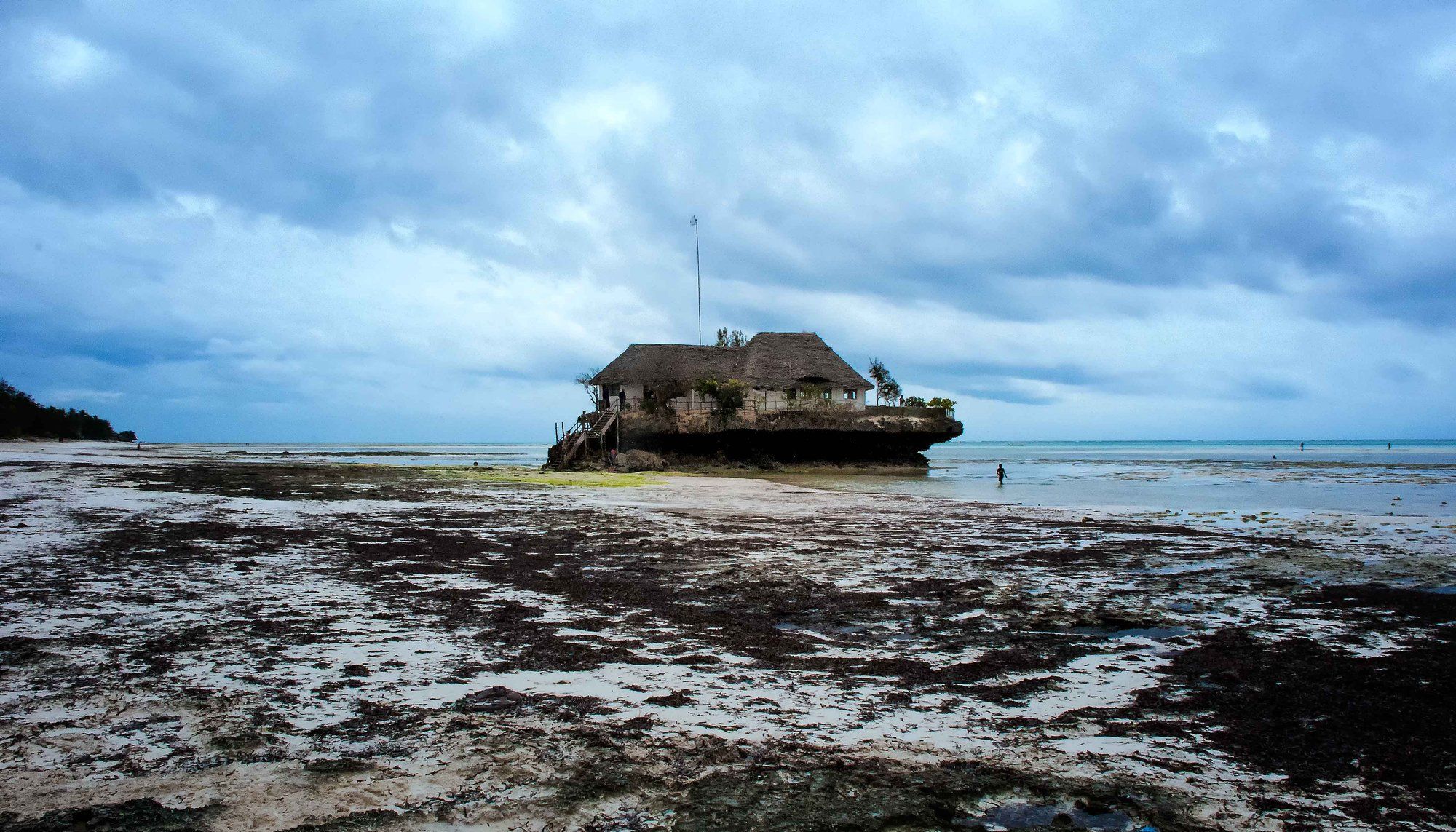 The Rock Restaurant perched on its coral outcrop off the Michamvi peninsula at low tide, the wide reef flat exposed across the foreground, the island's most photographed table and its signature splurge meal, on Zanzibar's southeast coast.