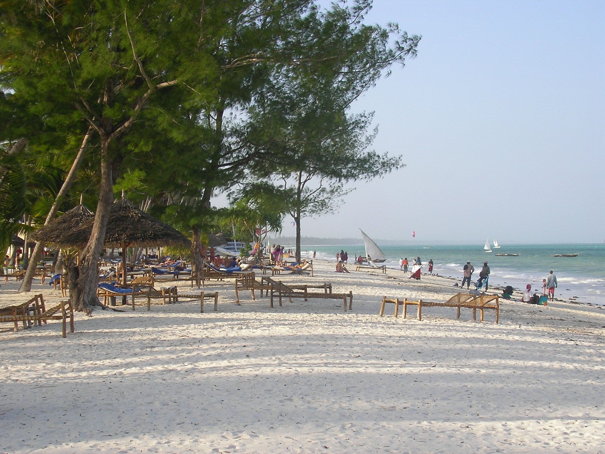 Sun-loungers and thatched umbrellas under palms on a Zanzibar resort beach, typical of the island's beach-resort stays.