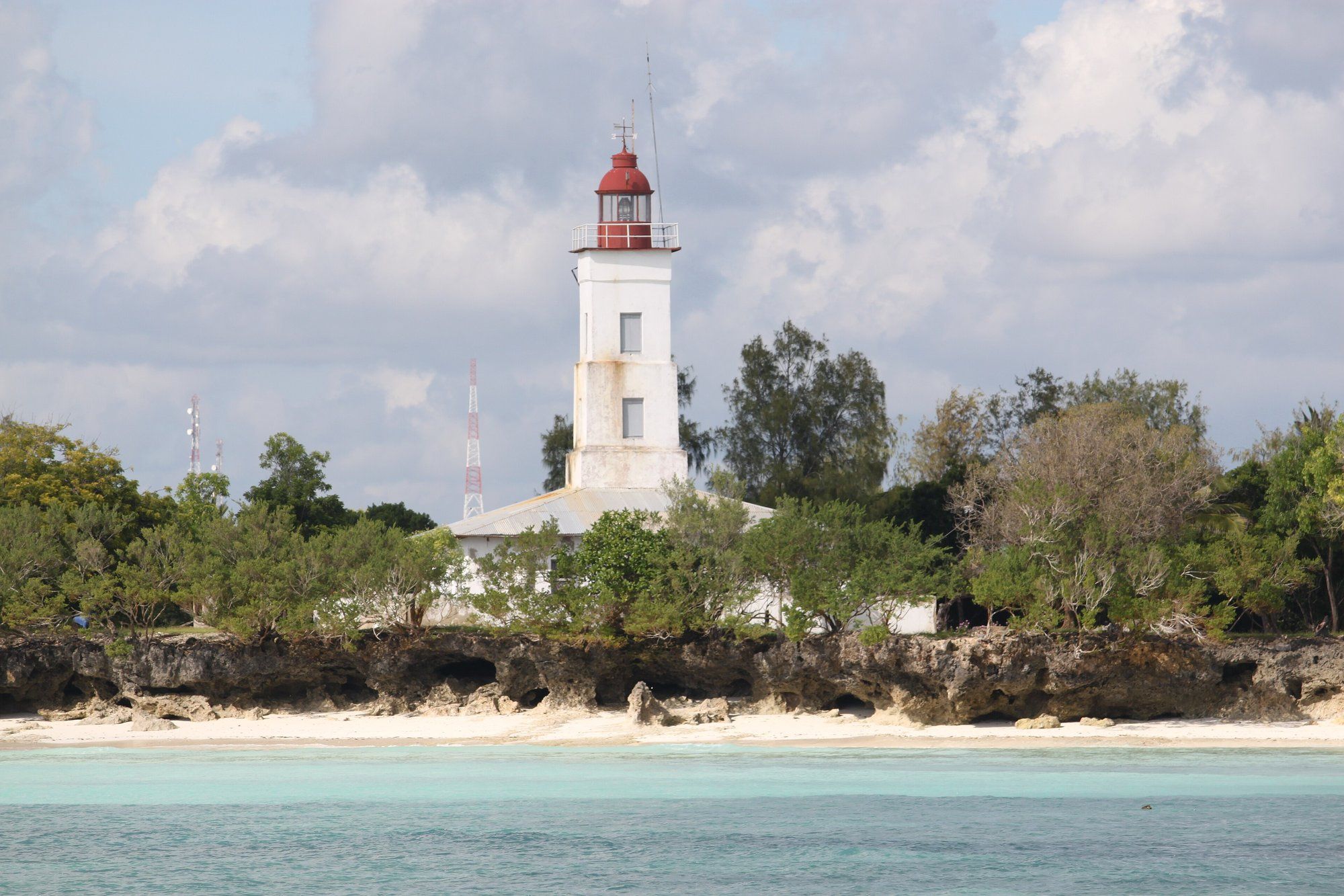 The lighthouse on the Ras Nungwi headland at the north tip of Zanzibar, turquoise water and a low coral cliff in the foreground, the swim-anytime north coast where the tide barely moves.