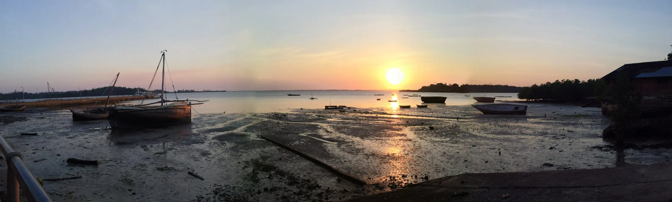 The harbour at Wete, one of Pemba's main towns, wooden boats resting on the tidal flats at low tide under a warm sky.