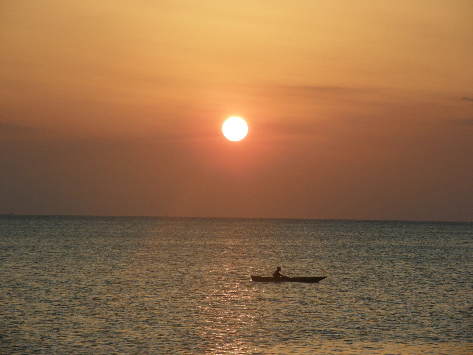 Sunset over the calm sea off Zanzibar's north coast near Kendwa, a lone paddler silhouetted on the water, the easy end-of-trip sunset the north is known for.