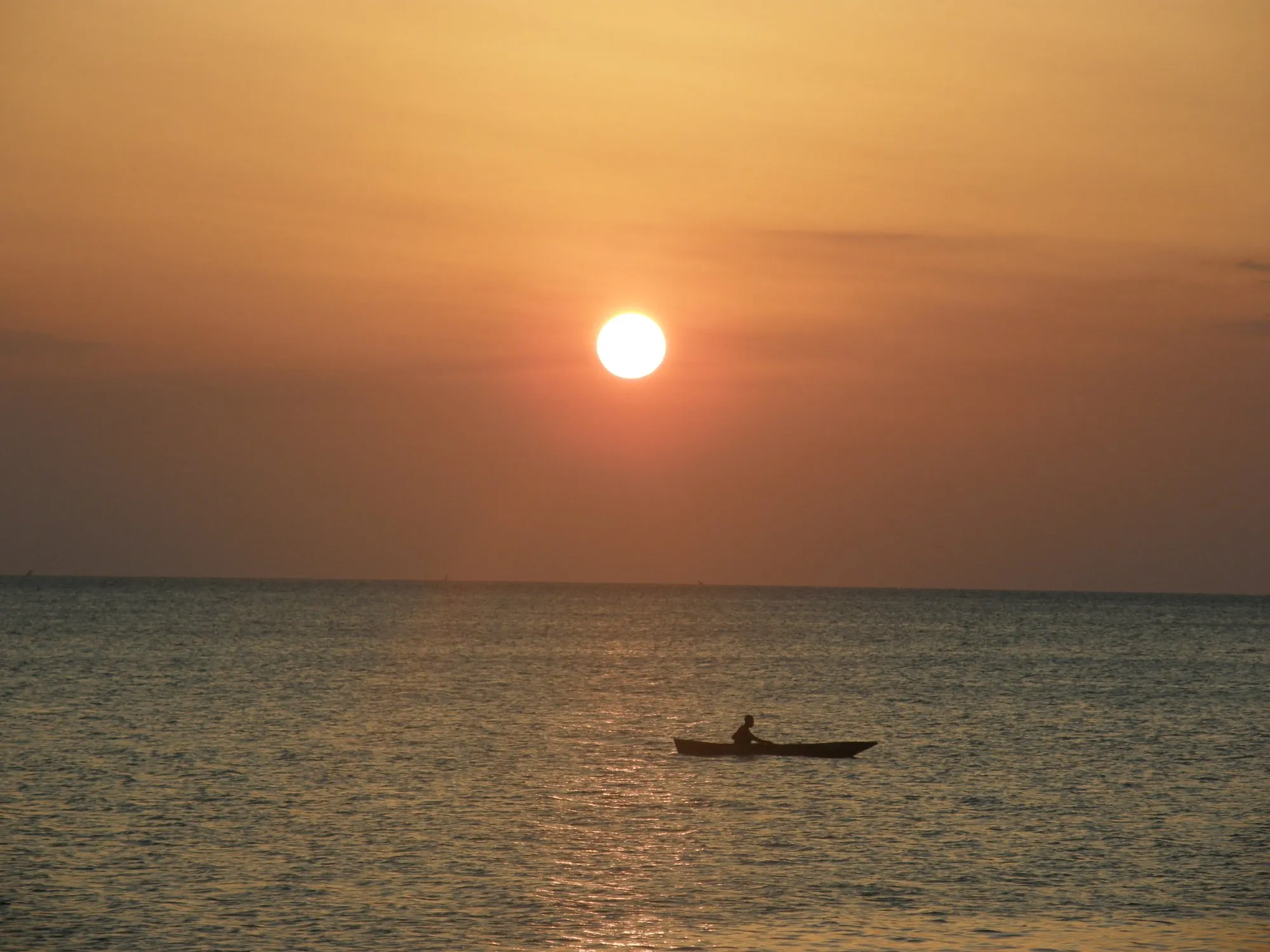 Sunset over the calm sea off Zanzibar's north coast near Kendwa, a lone paddler silhouetted on the water, the easy end-of-trip sunset the north is known for.