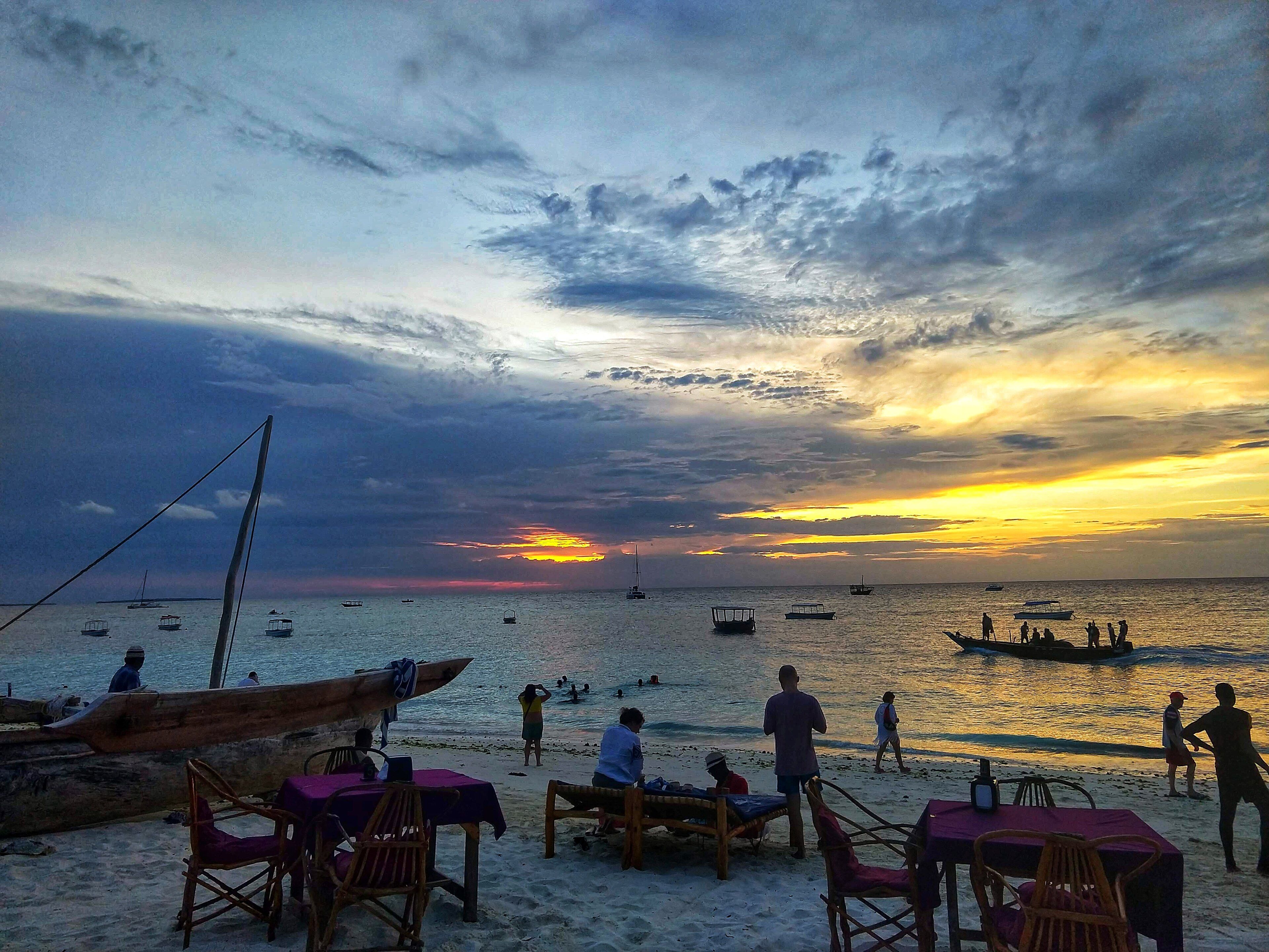 A lively beach-bar strip at sunset on Nungwi beach, dhows on the water under a dramatic golden sky, Zanzibar.