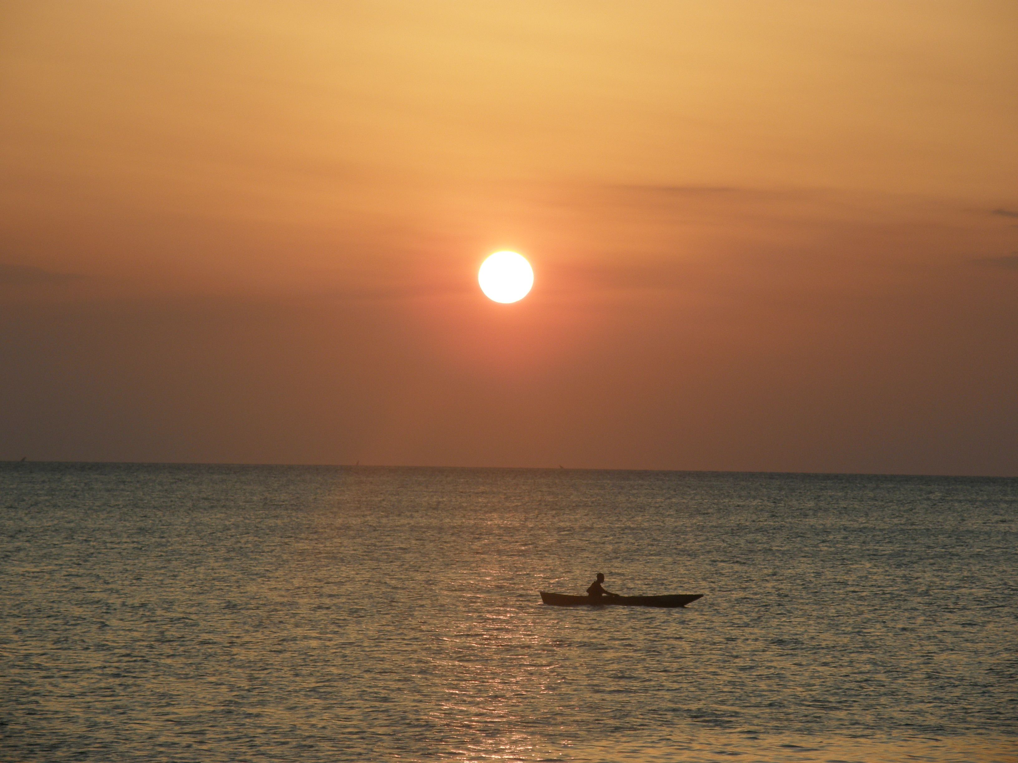 Sunset over the sea on Zanzibar's northwest coast near Kendwa, a lone paddler silhouetted on the calm water.