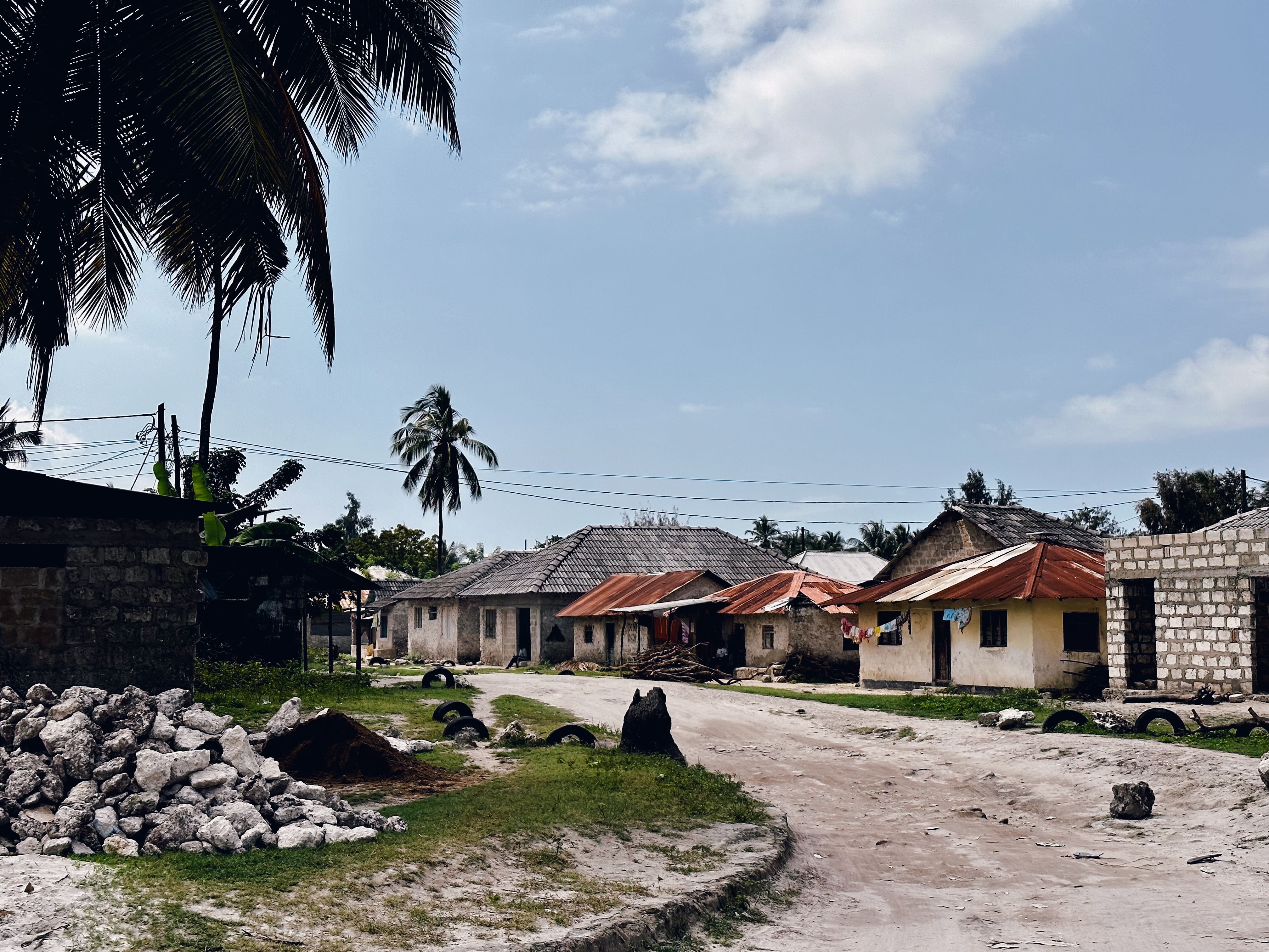 A sandy village lane at Matemwe lined with coral-rag and tin-roofed houses, coconut palms and a coral-rock wall, everyday life on Zanzibar's northeast coast.